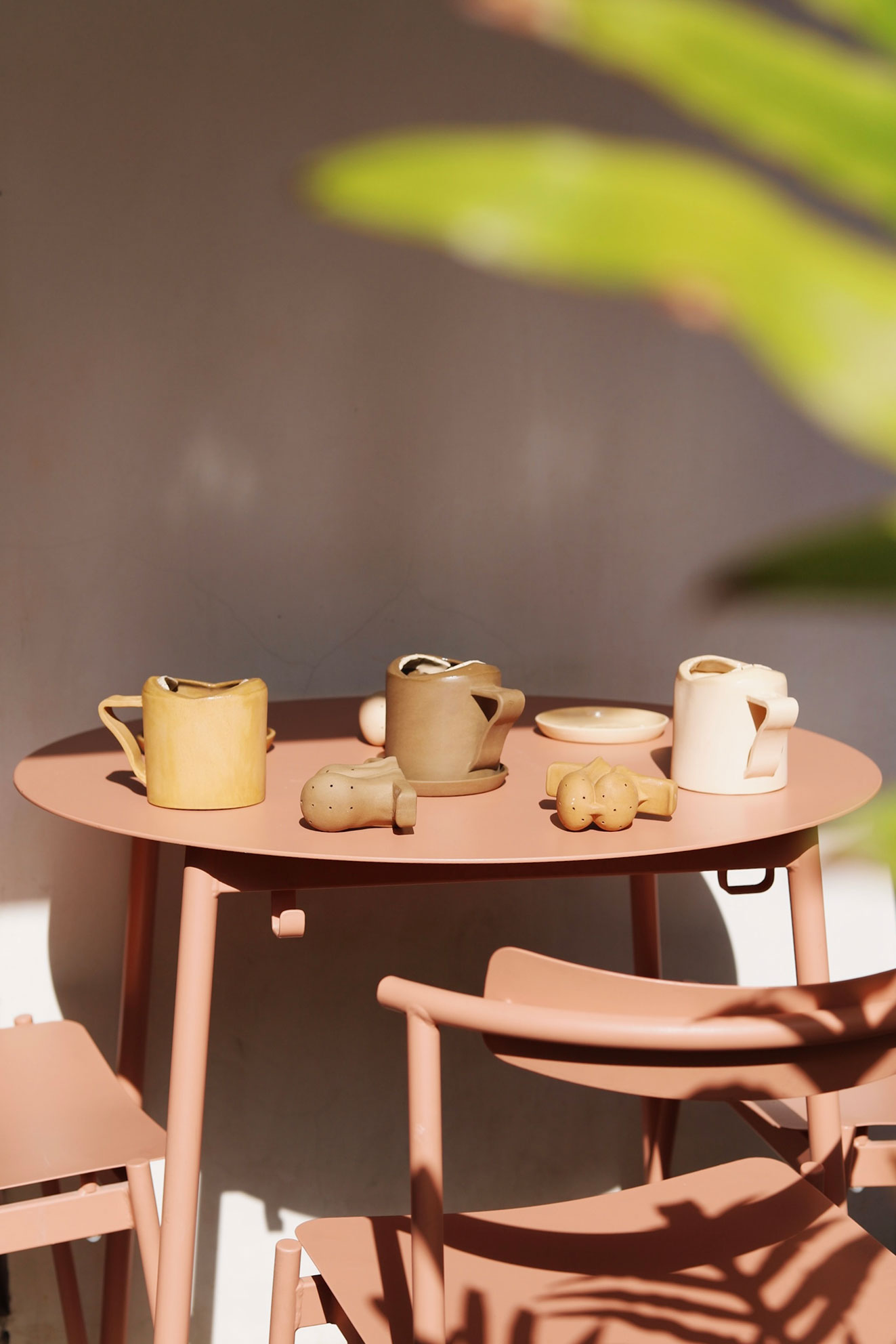 Terracotta table with three ceramic mugs and ceramic salt and pepper shakers in sunlight.