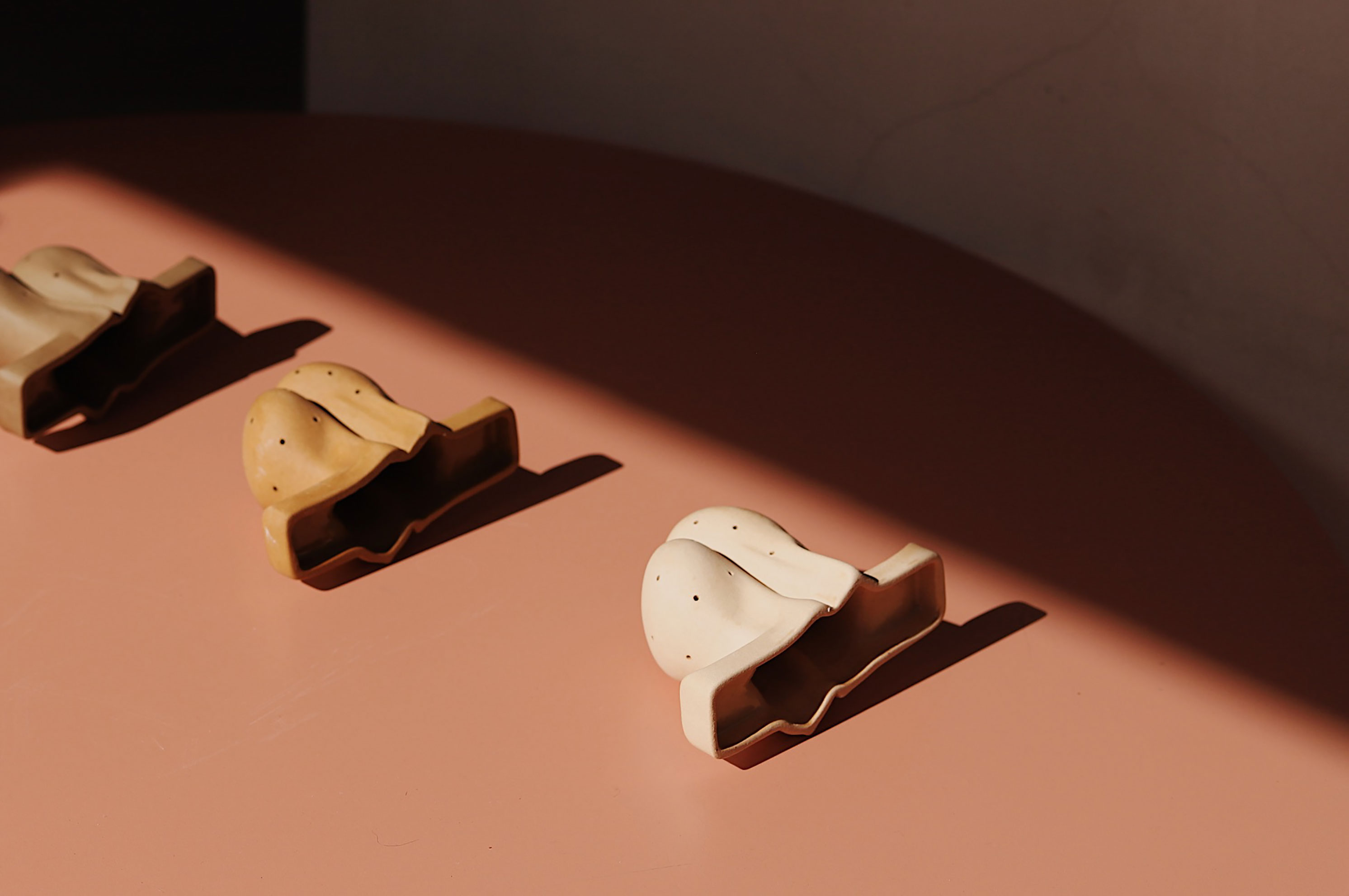 Three small ceramic objects shaped like shells, arranged diagonally on a brown surface.