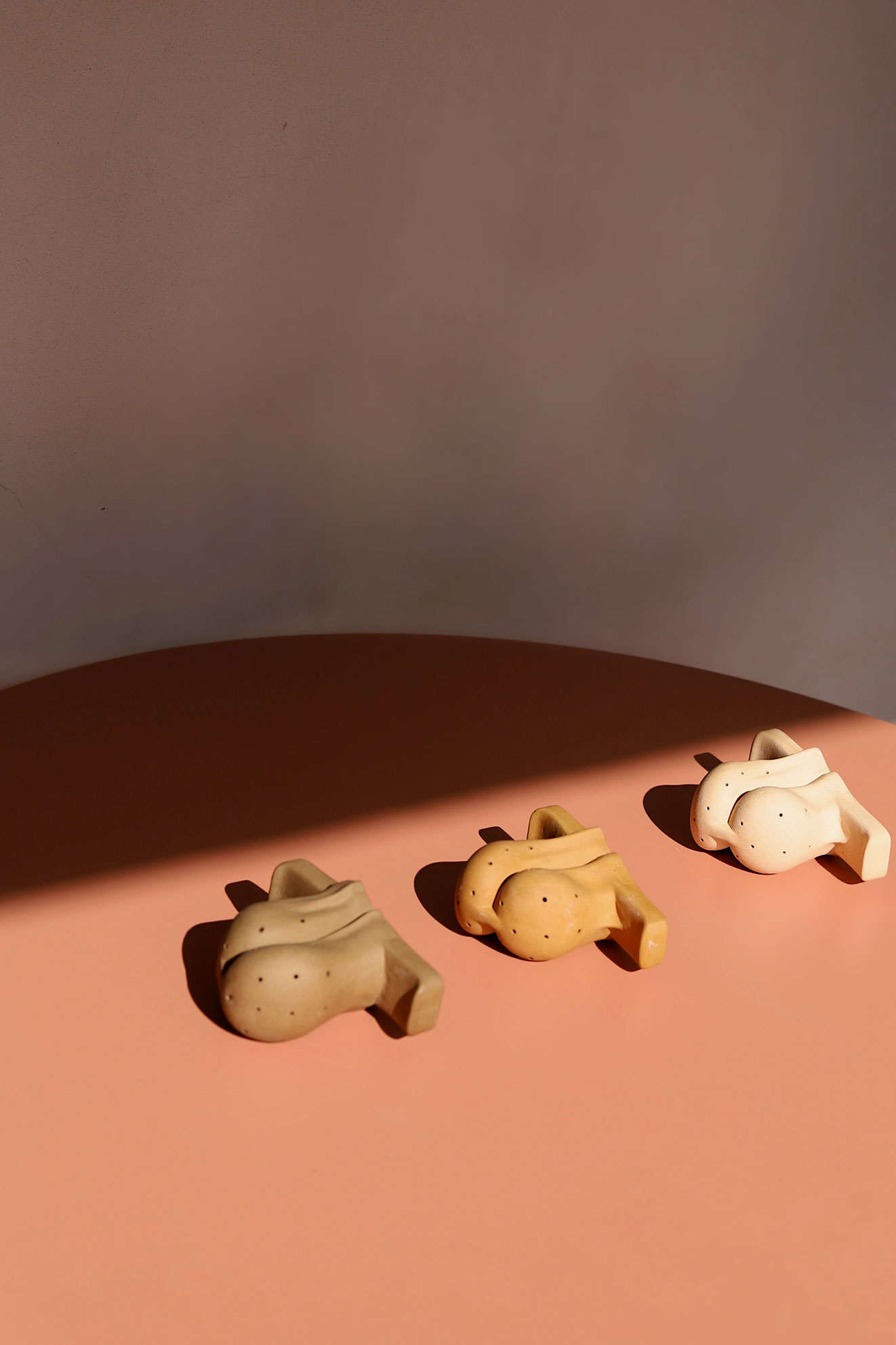 Three ceramic sculptures shaped like abstract bodies with polka dots on a pink surface under soft light.
