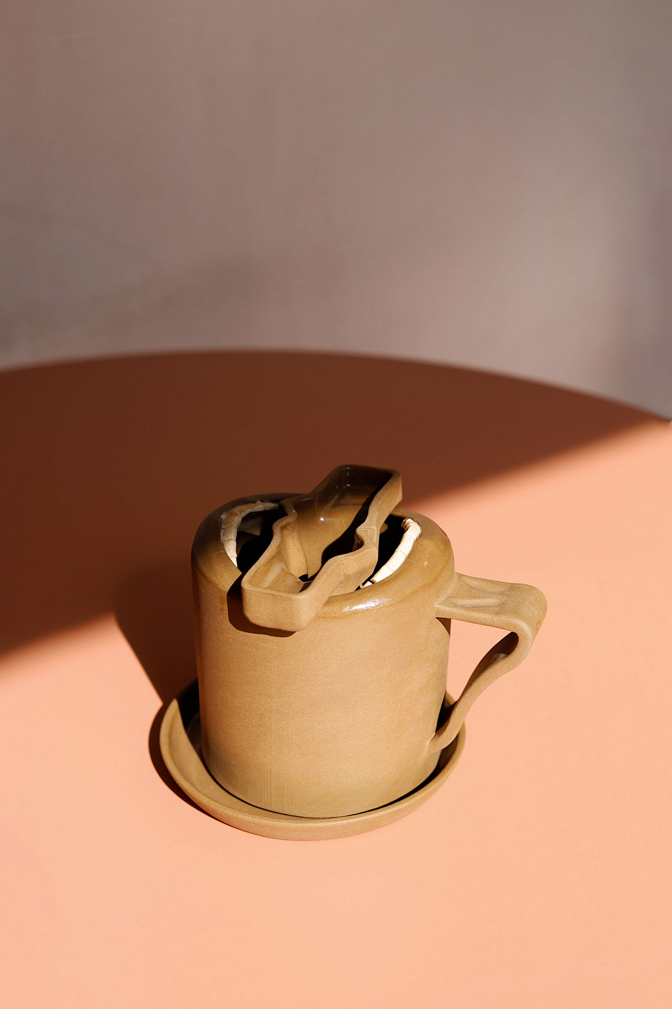 Brown ceramic mug with a saucer and a coffin-shaped cookie cutter on top, casting shadows.