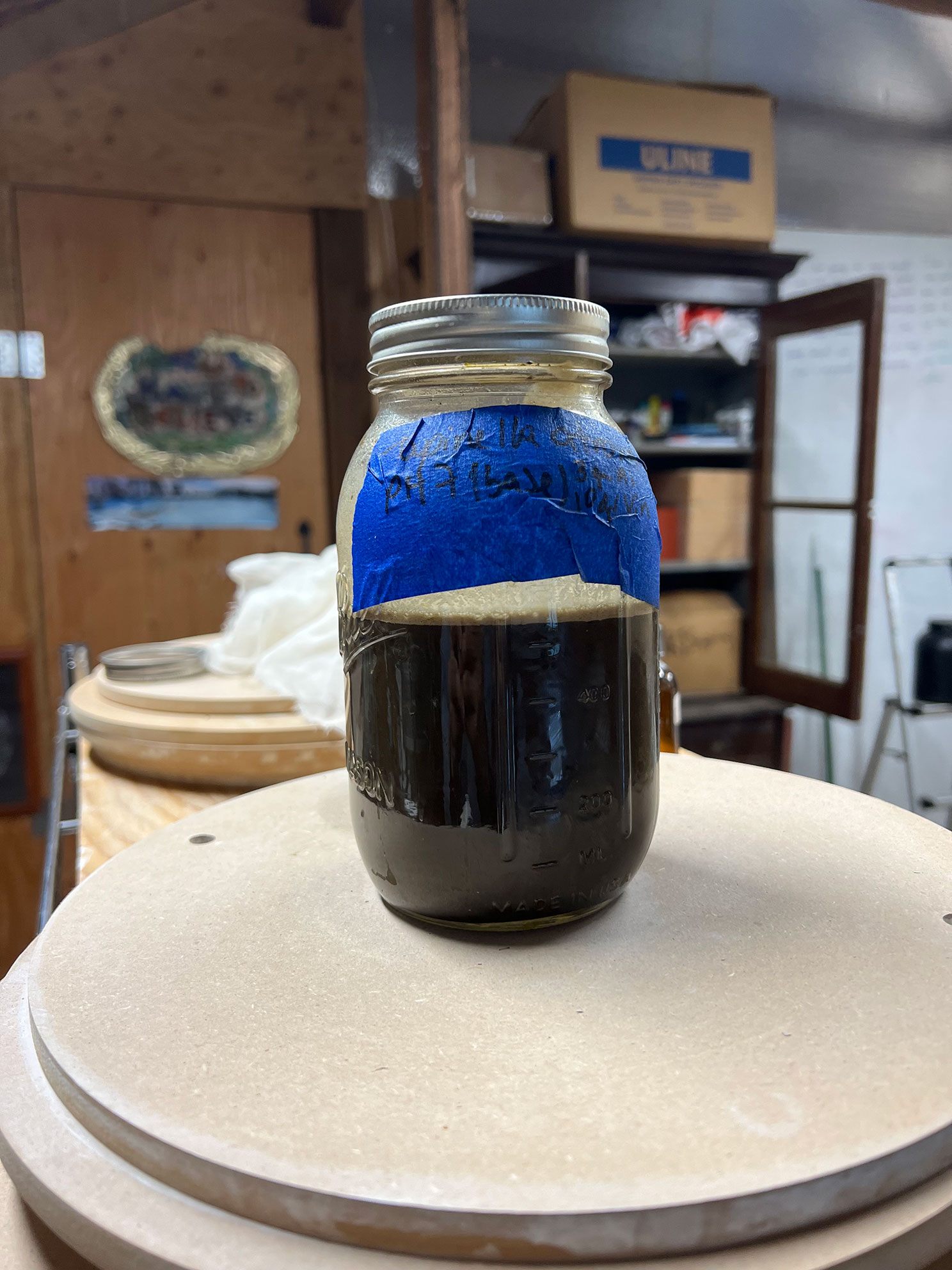 Glass jar filled with dark liquid and sealed with metal lid on a round wooden surface.