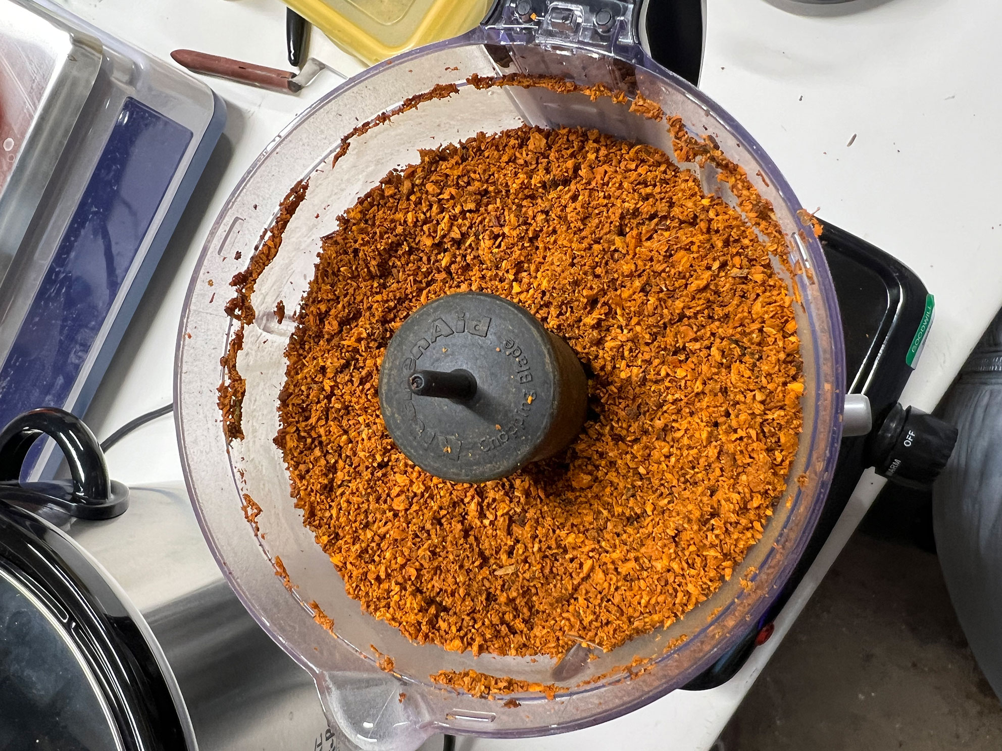 Food processor bowl filled with finely chopped orange substance on a kitchen counter.