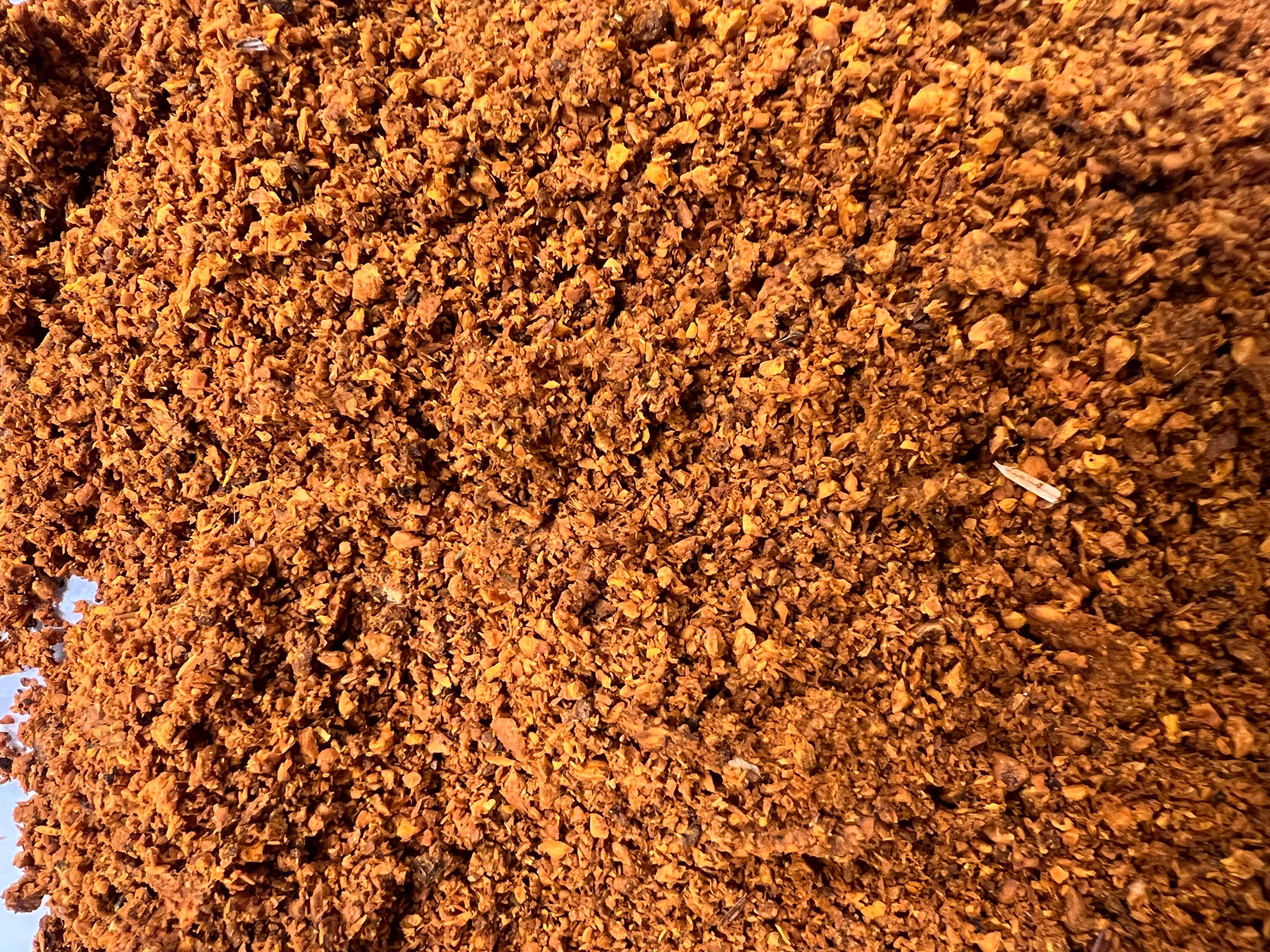 Close-up of loose, brown ground coffee beans with varied texture and small fragments.