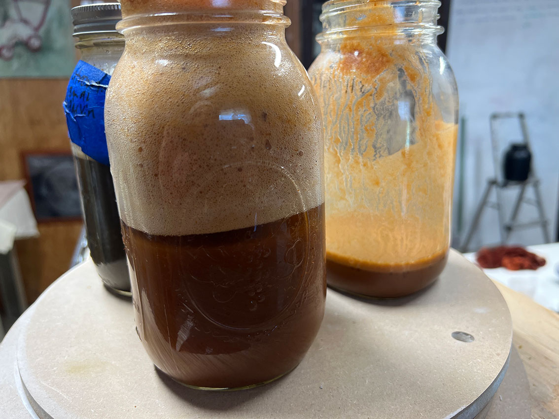Three glass jars on a table, one with dark liquid and foam rising inside it.