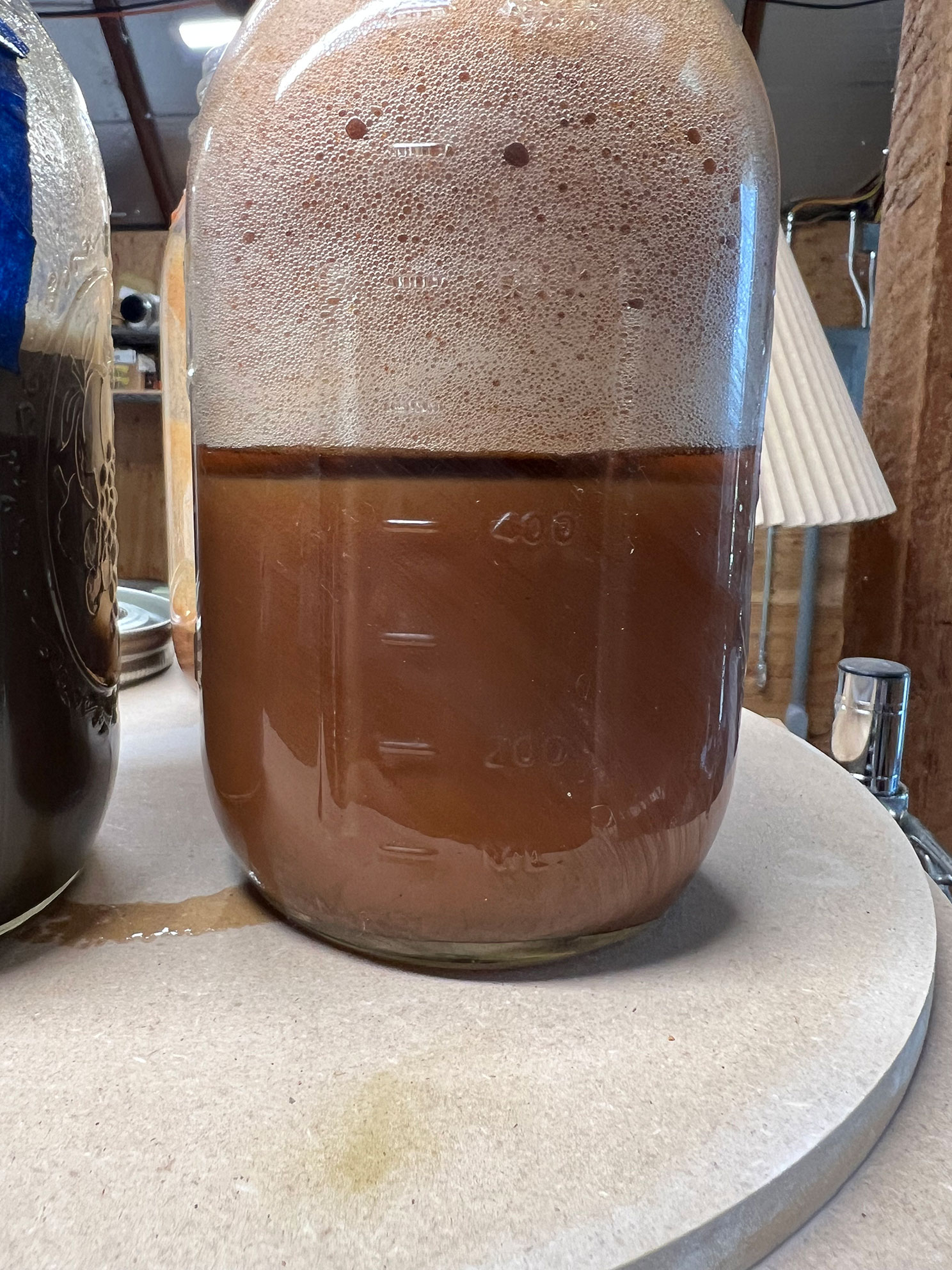 Glass carboy partially filled with dark brown liquid and foam on top, on a round table.