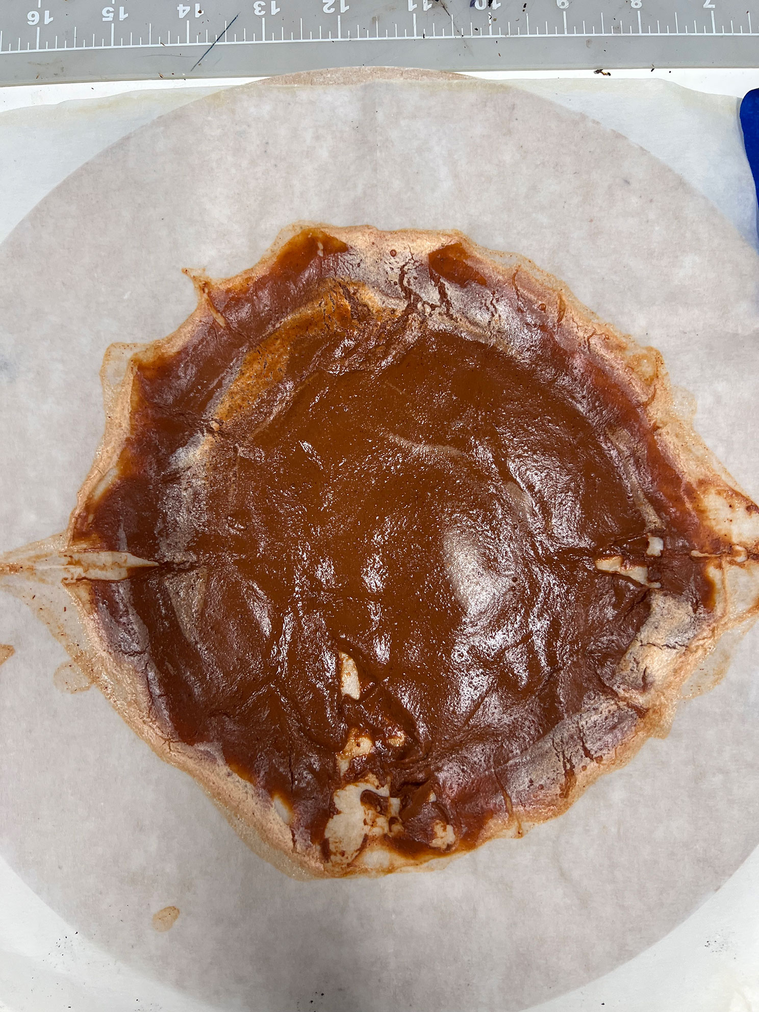 A sticky brown resin spread on parchment paper with a ruler above it for scale.
