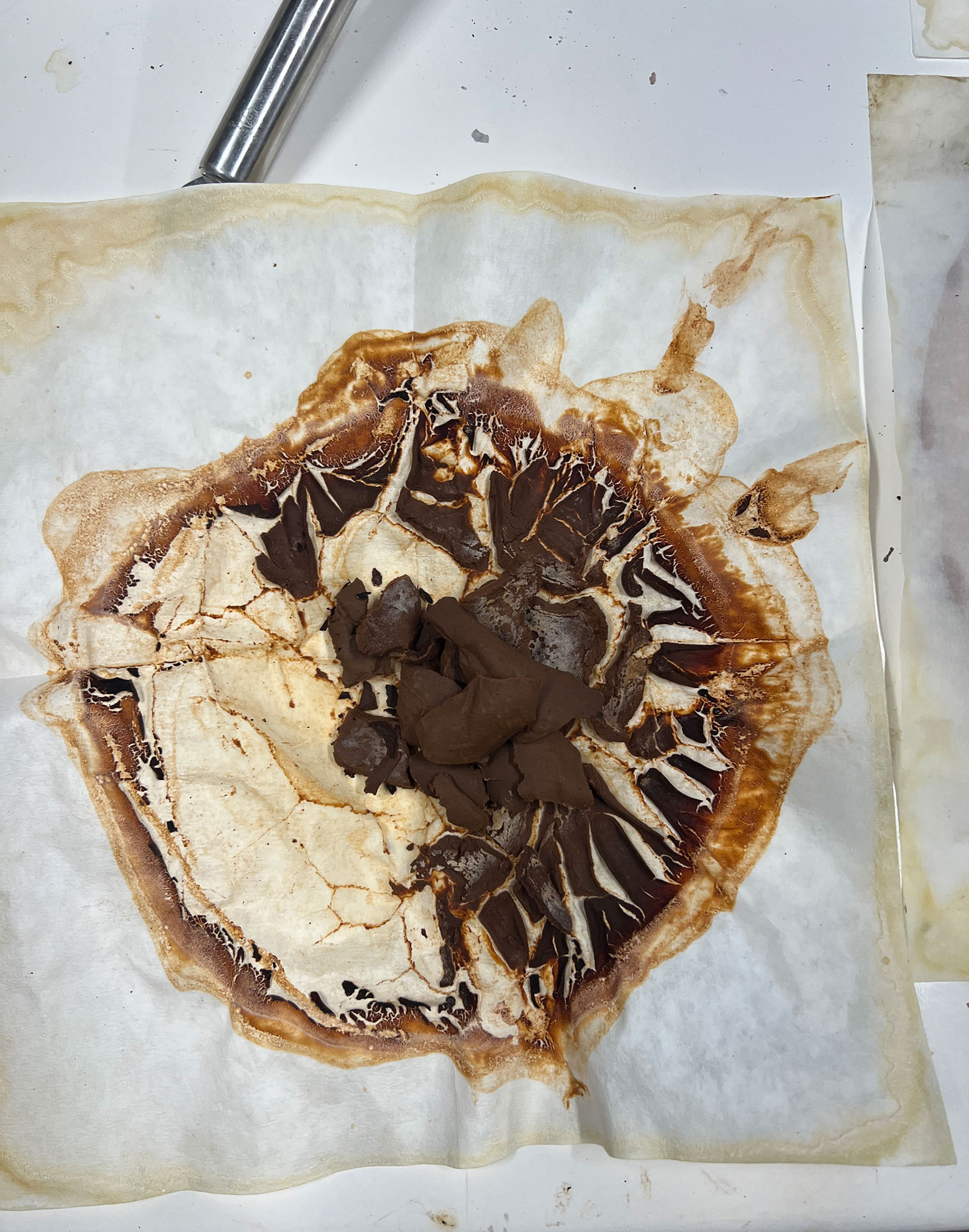 Burnt and cracked dark brown material on white parchment paper on a surface.
