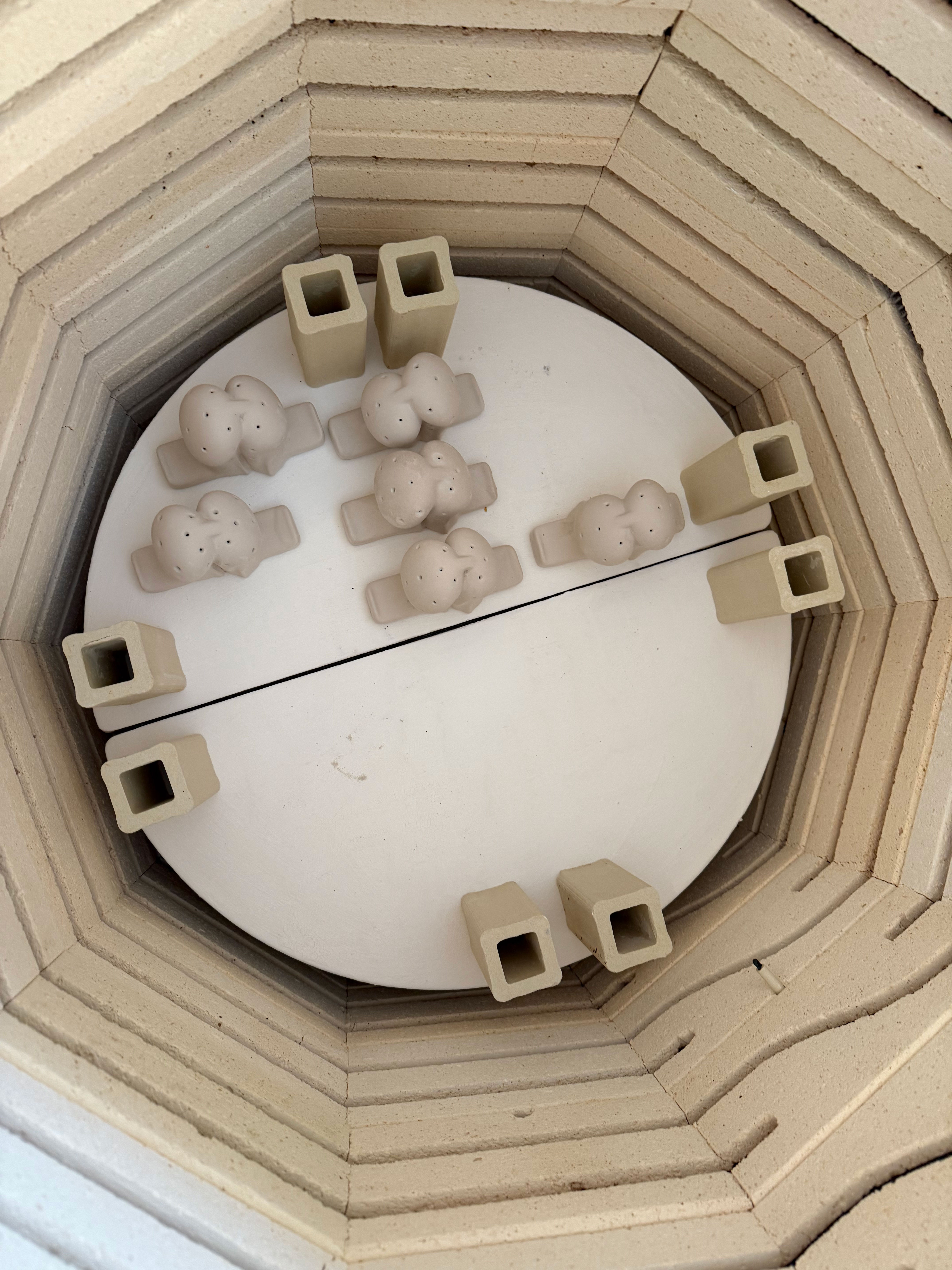Top view inside a ceramic kiln with clay pieces arranged on a circular shelf.