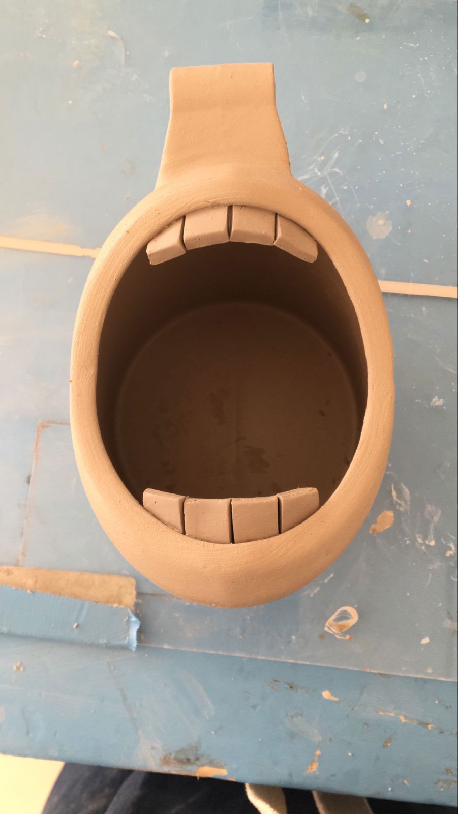 Unpainted clay pot shaped like a face with rectangular teeth along the opening.