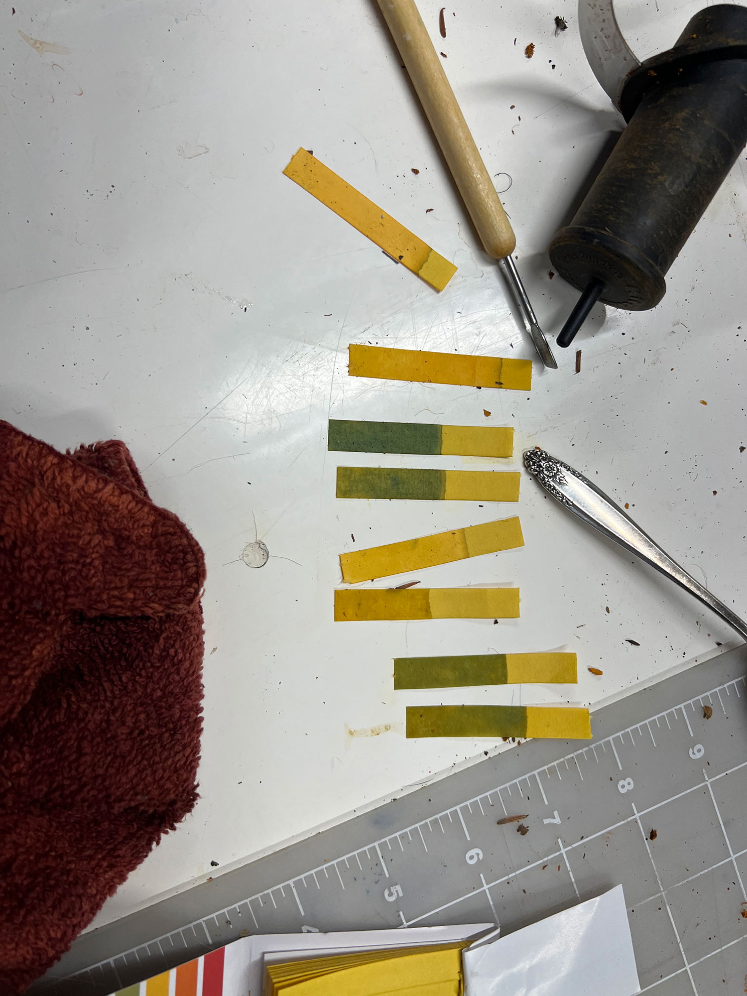 Yellow and green pH test strips on a white surface with tools and a red cloth nearby.